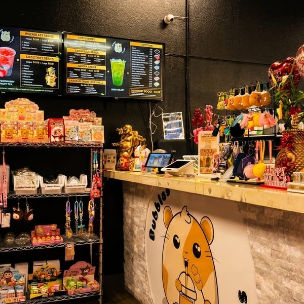 A boba tea shop interior with a counter, menu screens, and shelves displaying drinks and merchandise.