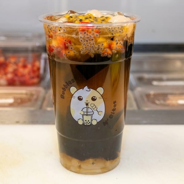 A clear plastic cup of Bubbles N' Bites boba tea with fruit, basil seeds, and jelly.