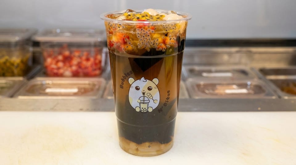 A clear plastic cup of Bubbles N' Bites boba tea with fruit, basil seeds, and jelly.