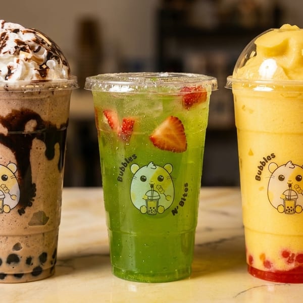 Three colorful bubble tea drinks from Bubbles N' Bites: chocolate, green tea with strawberries, and mango.