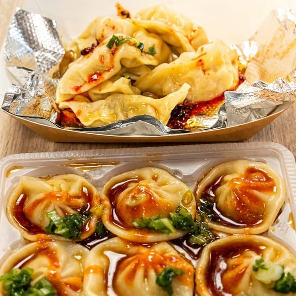Two containers of dumplings, one with chili oil and the other with sauce and green onions.