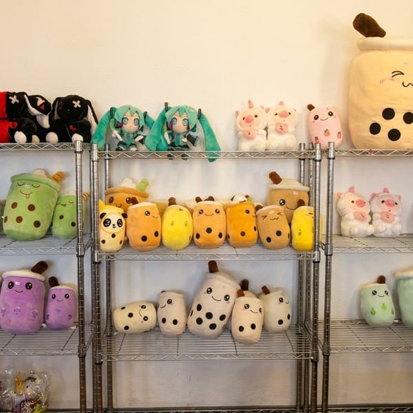 A metal shelving unit displays rows of various boba tea, animal, and character plush toys.