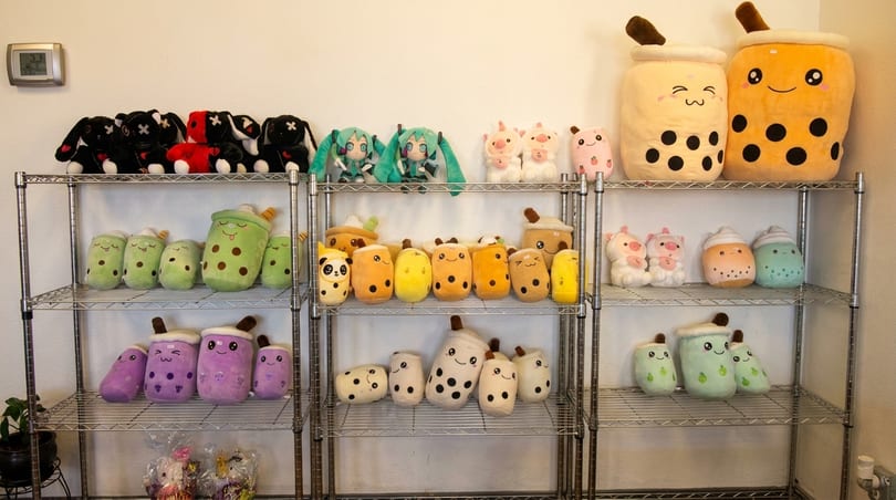 A metal shelving unit displays rows of various boba tea, animal, and character plush toys.